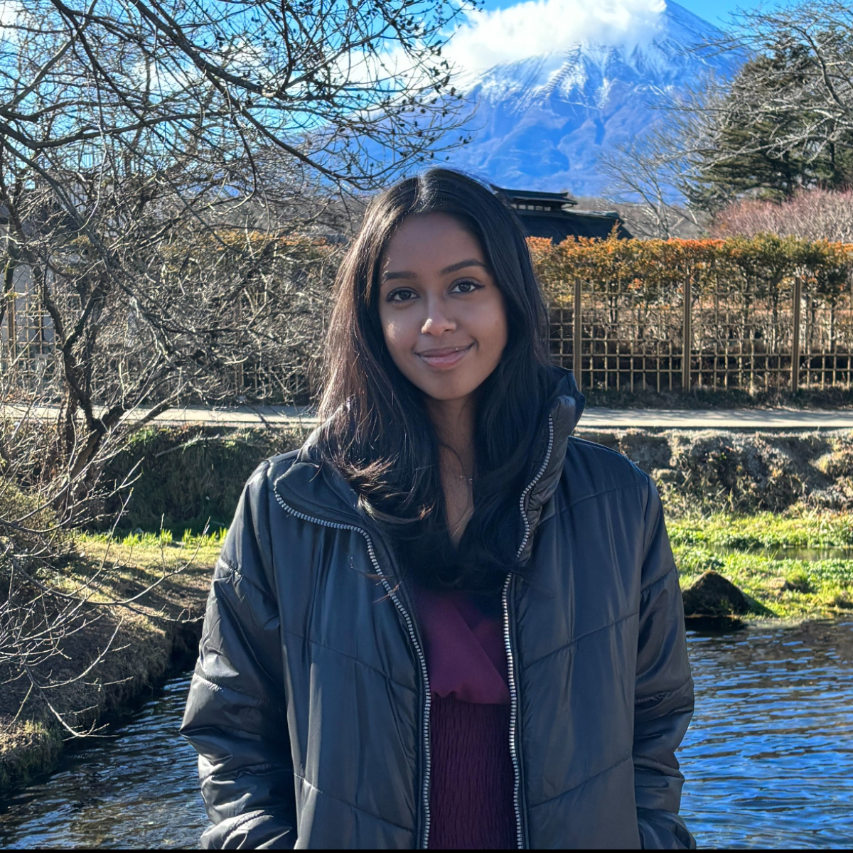 Anusha smiles outdoors in front of a small pond.