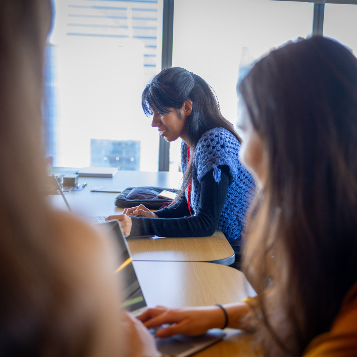 Three women work on laptops at a large table.